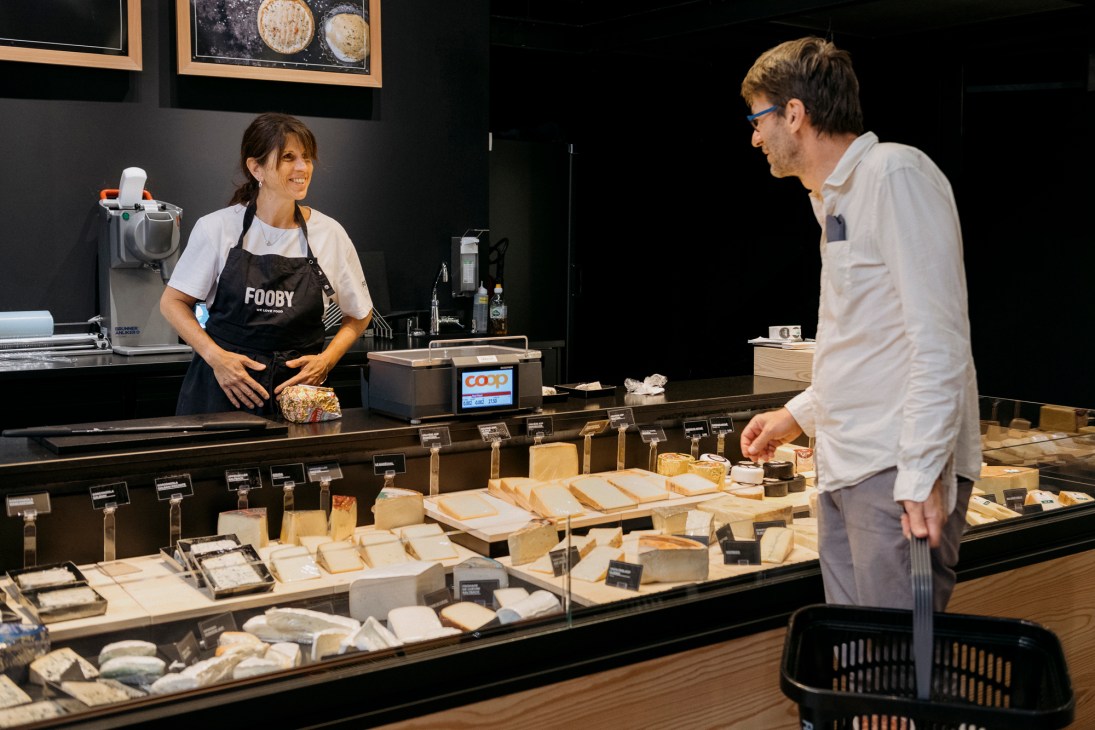 Woman in black Fooby apron serving customer at upscale cheese counter display