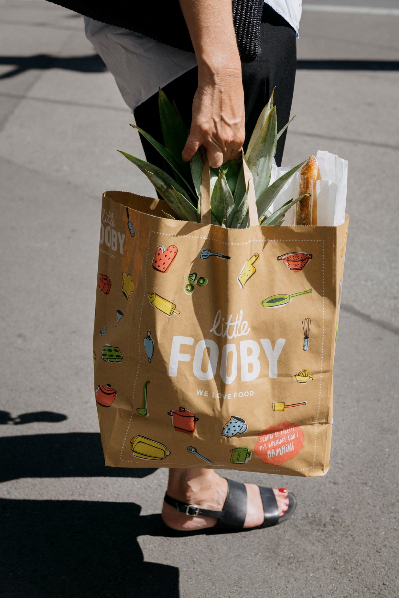 Brown paper shopping bag from Little Fooby filled with groceries including leafy greens and baguette