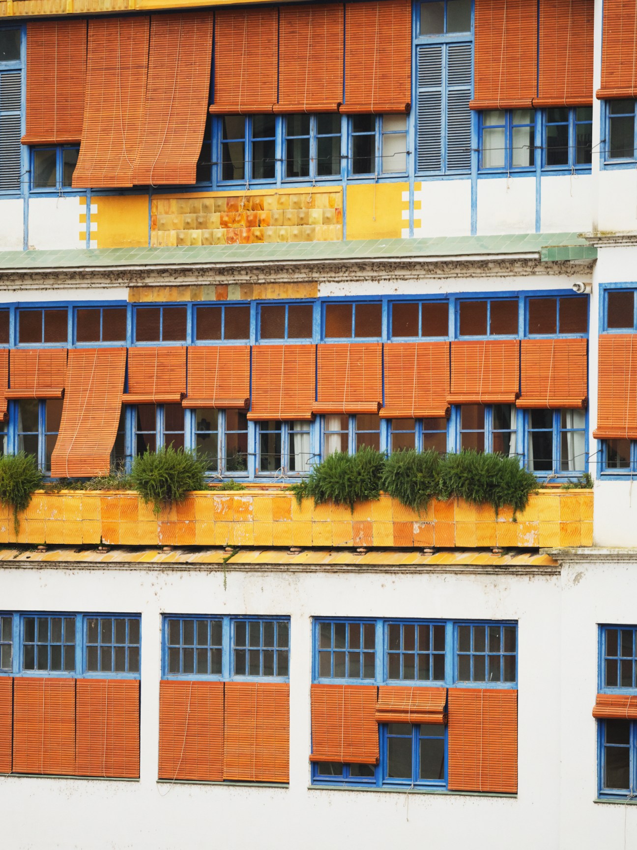 Colorful mid-century building facade with orange shutters, blue window frames and yellow geometric details.