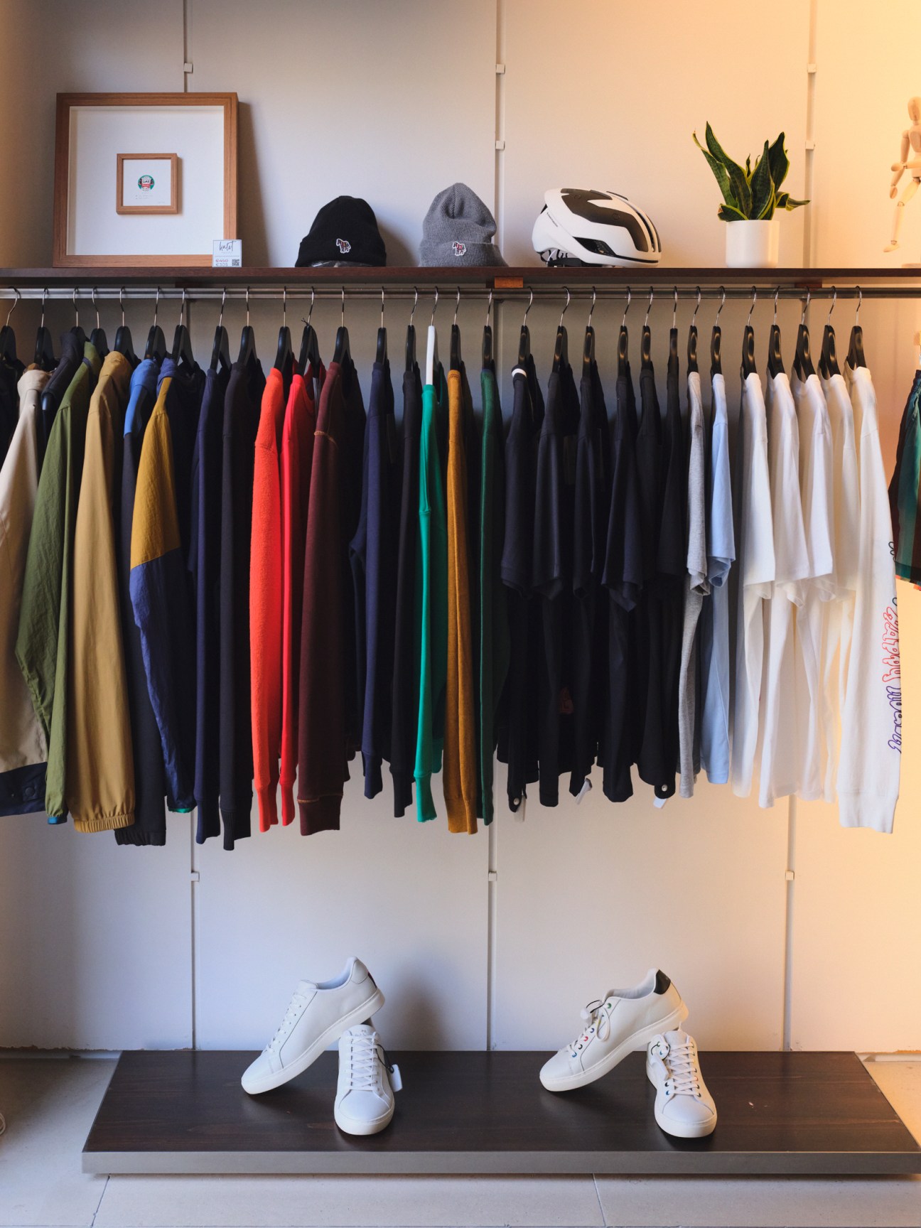 Clothing boutique display with colorful garments on hangers and white sneakers on shelf below