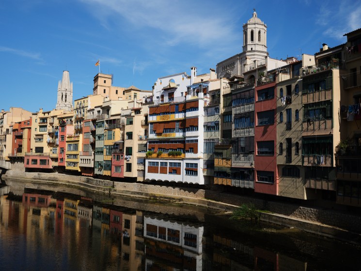 Colorful residential buildings reflected in calm water along Girona's riverfront in Spain.