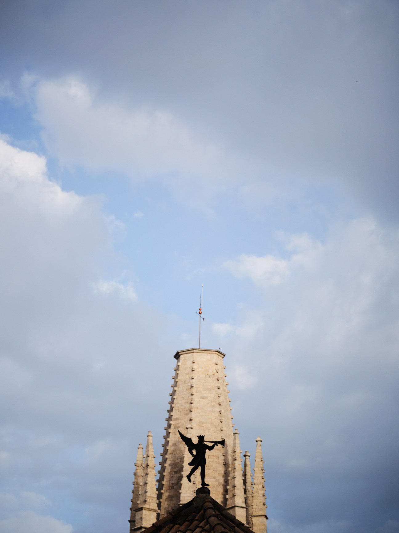 Silhouette sculpture of a figure balanced on a rooftop against stone church spires and blue sky