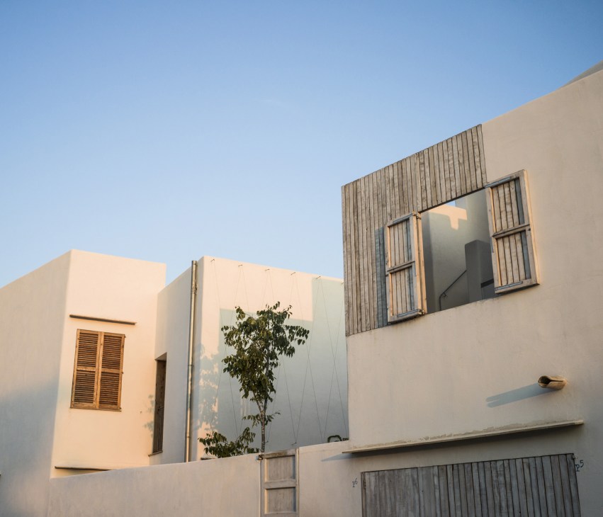 Exterior of a modern white residential building with wooden vertical slat detailing and large windows under clear blue sky.