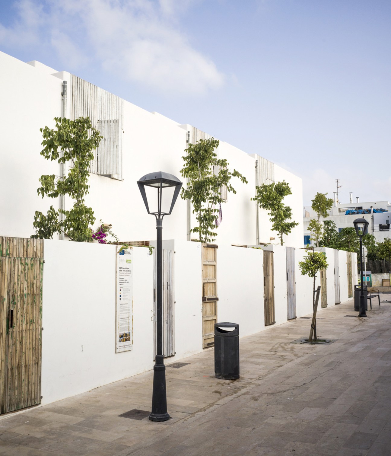 White modular housing buildings with wooden doors and climbing vines on a pedestrian street in Formentera, Spain.