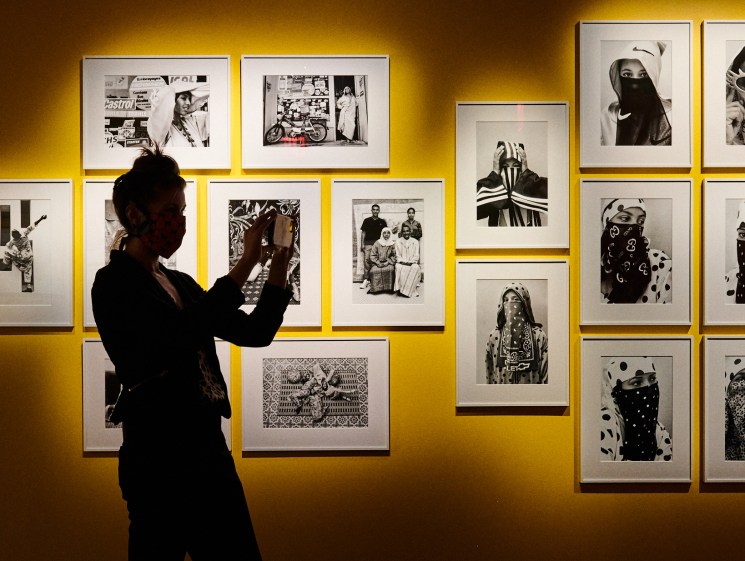 Person in dark clothing viewing framed black and white photographs on yellow-lit gallery wall at Fotografiska New York