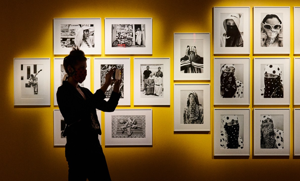 Person in dark clothing viewing framed black and white photographs on yellow-lit gallery wall at Fotografiska New York