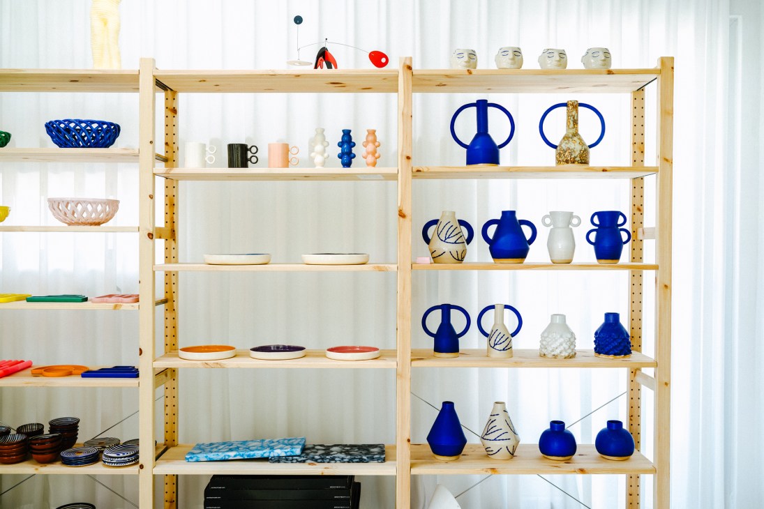 Wooden shelving displays colorful ceramic vases, bowls and home décor items including blue vessels and patterned ceramics.