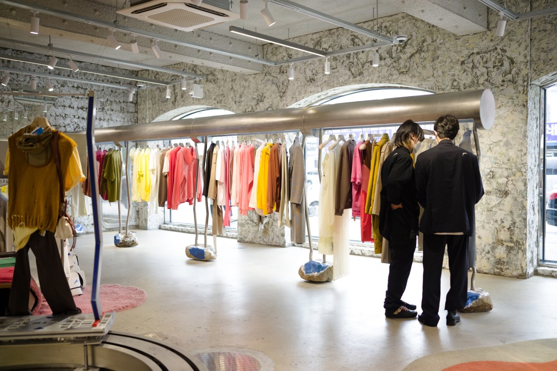 Customers browse colorful clothing displayed on racks in a minimalist Seongsu boutique with raw concrete walls.