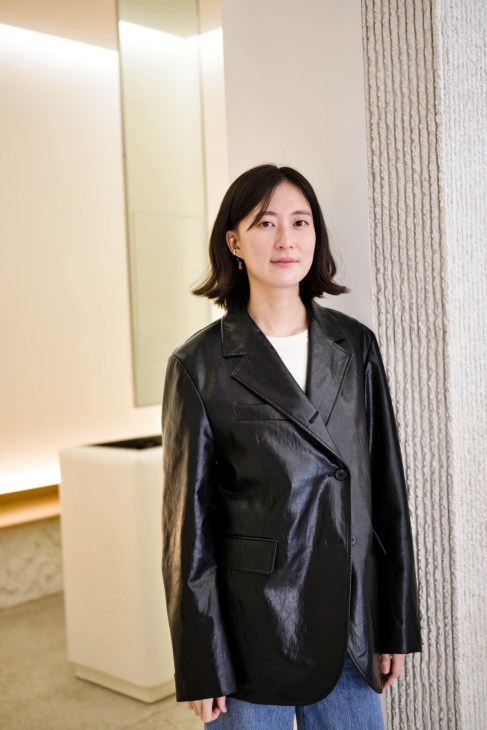 Jiyoon Yun, creative director of eyewear brand Yun, standing in a minimalist interior space wearing a black blazer.
