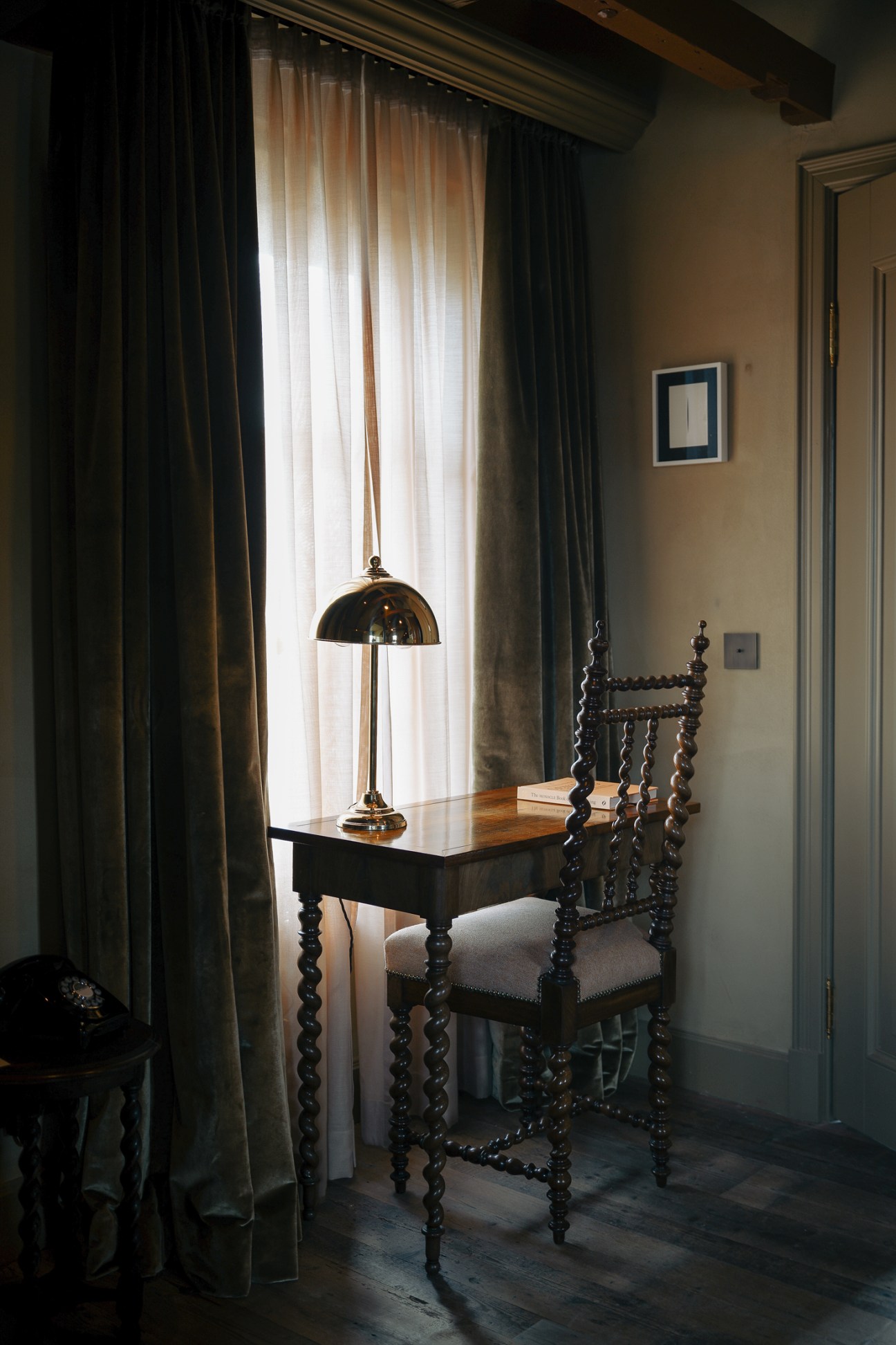 Traditional barley twist wooden chair and desk positioned by large window with curtains overlooking lake view