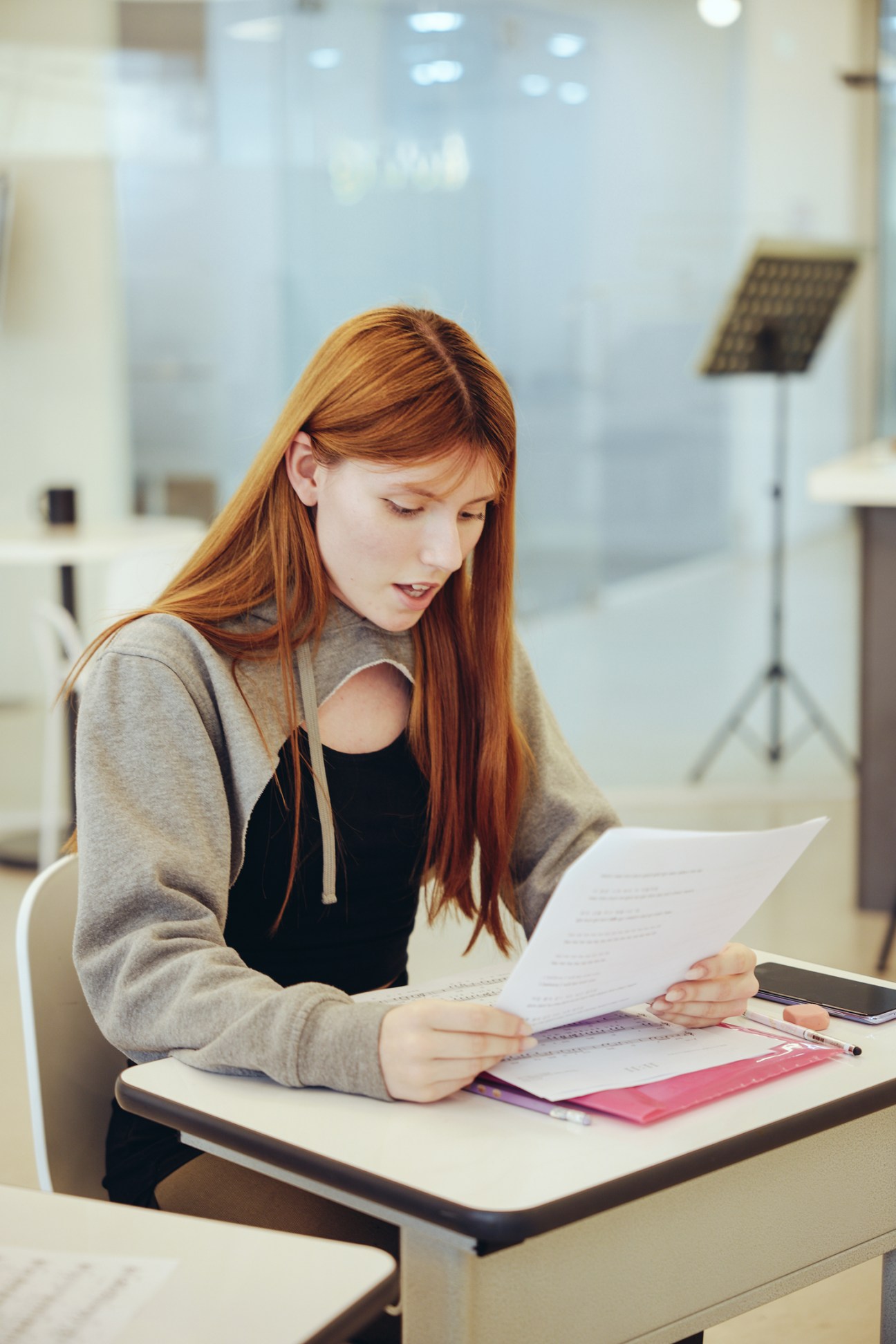Young woman with long reddish hair reading papers at a desk in a bright modern interior