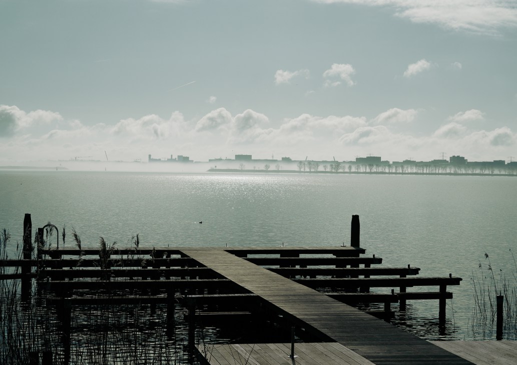 Wooden jetty extending into Ijmeer lake with Amsterdam skyline visible in misty distance