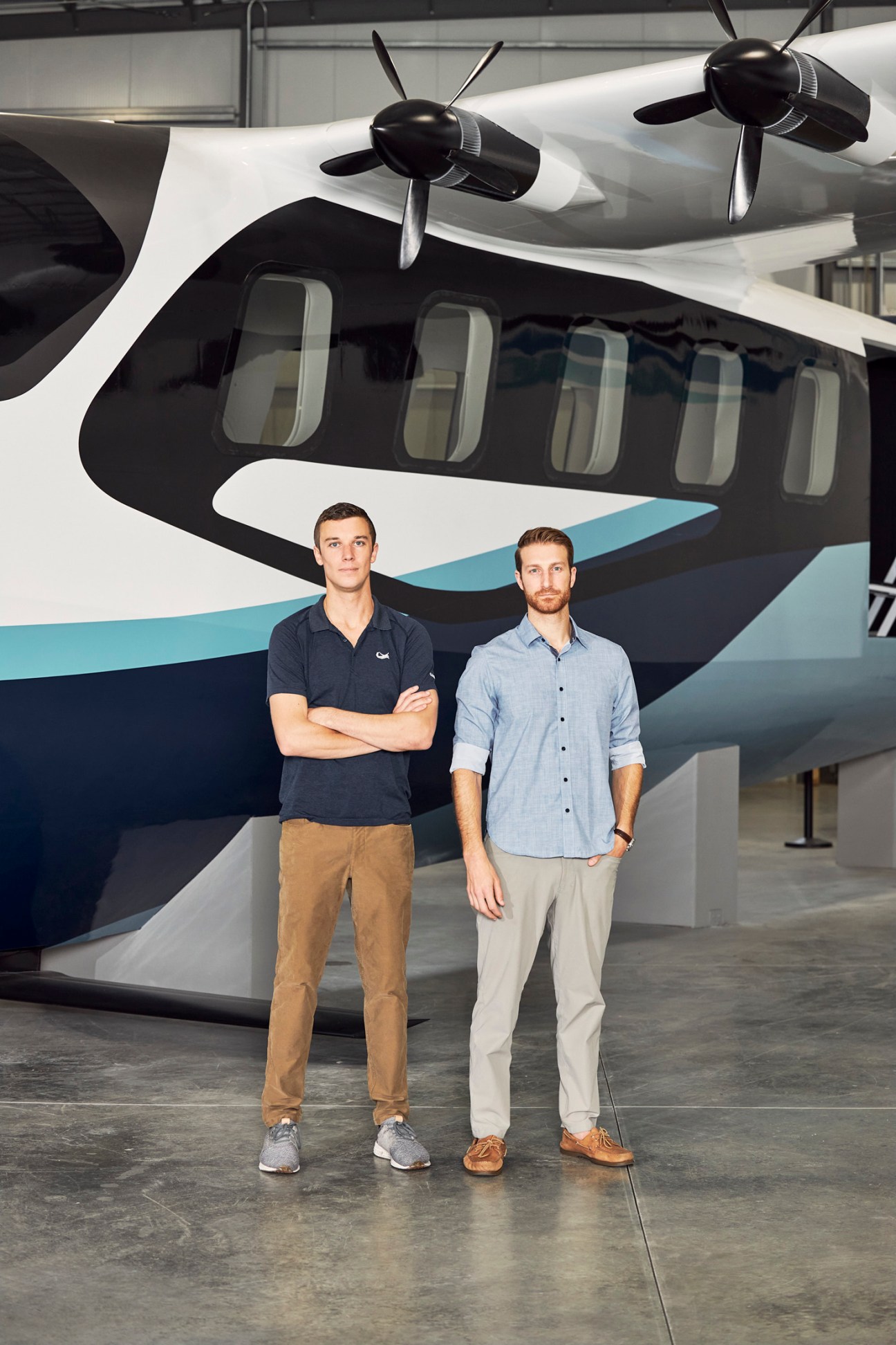 Two men standing in front of a white and blue twin-engine aircraft in a hangar