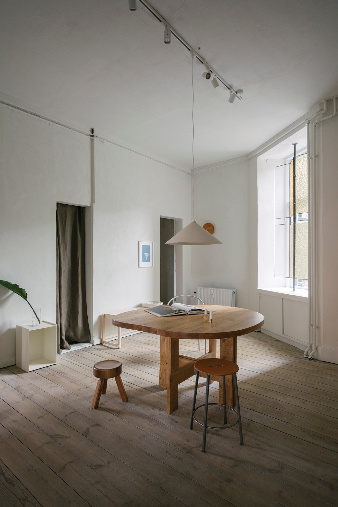 Minimalist dining room with wooden round table, track lighting, and white walls in modern interior