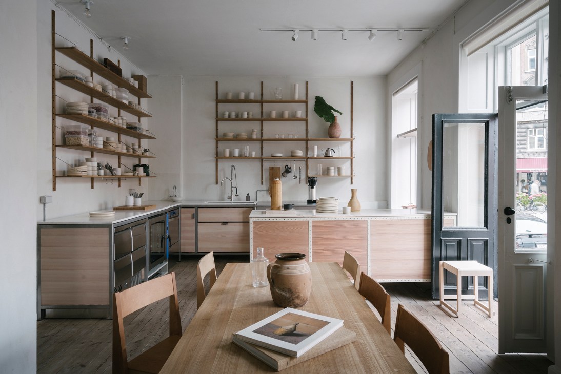 Minimalist kitchen and dining area with wooden shelving, light wood cabinetry, and dining table