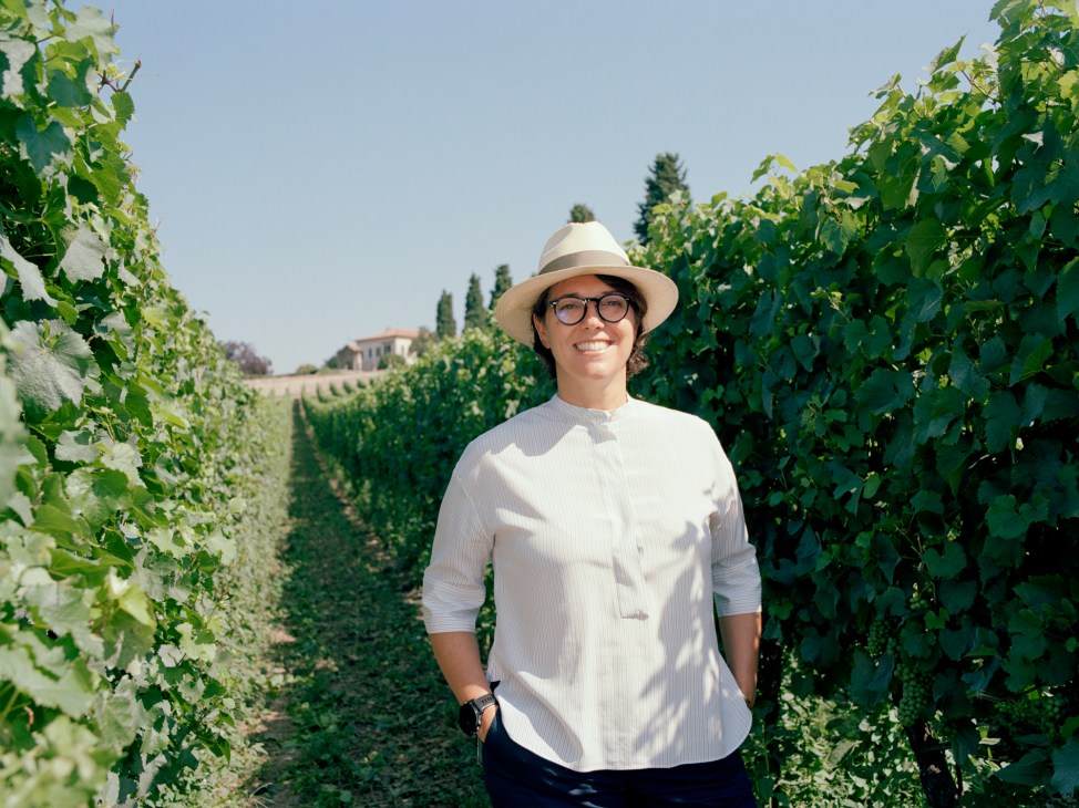 Francesca Moretti standing in a vineyard wearing a white hat and shirt, smiling at the camera