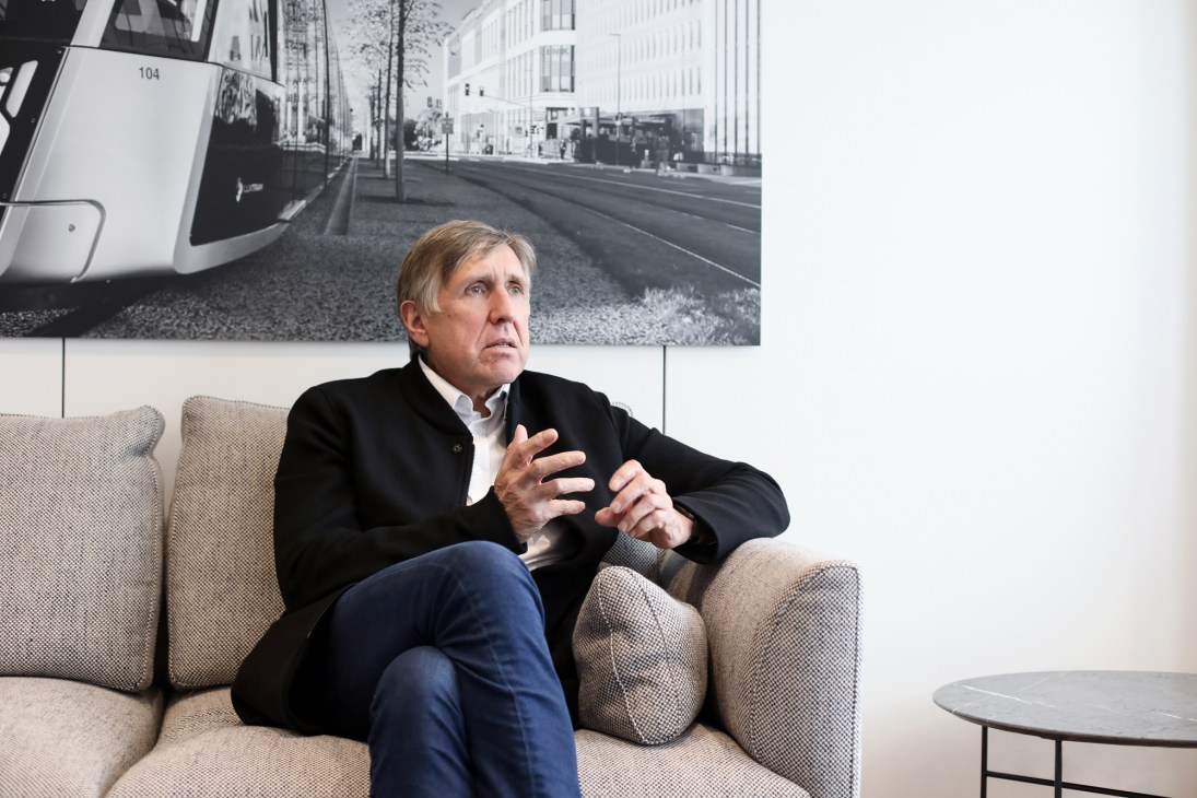 François Bausch sitting on a beige sofa in a modern office setting with a black and white cityscape photo behind him