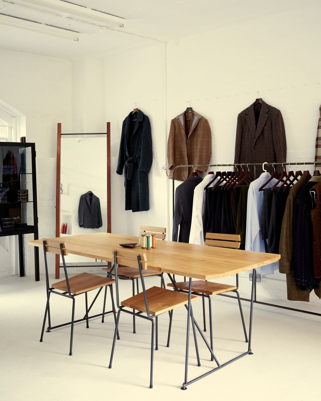 Interior of Fred Nieddu's Shoreditch tailoring studio with wooden workbench, chairs, and suits on display