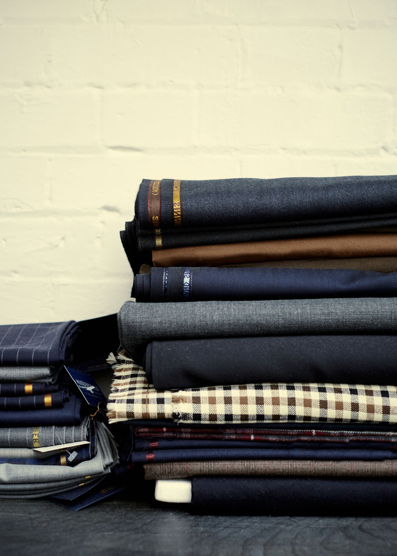 Stacked folded suit fabrics in various colors and textures with gold trim details.