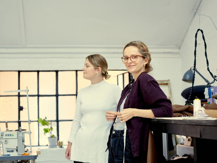 Two women working on tailoring projects at workbenches in Fred Nieddu's Shoreditch studio.