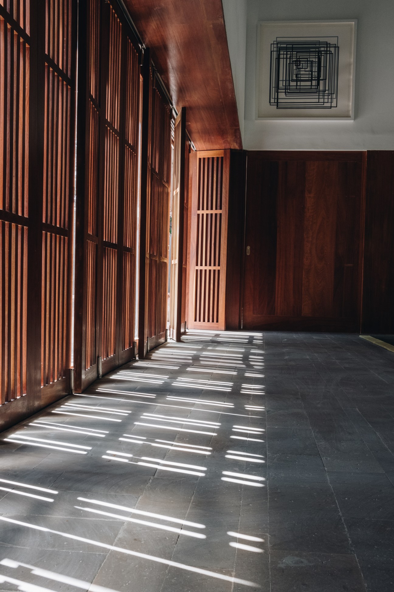 Interior hallway with wooden slatted walls and dramatic striped shadows from sunlight filtering through sliding panels