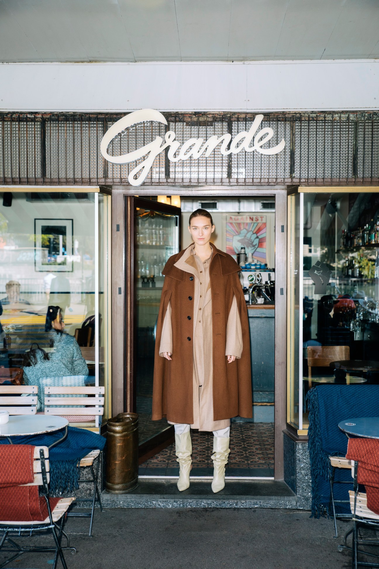 Model in brown layered coats standing in doorway of Grande cafe in Zürich