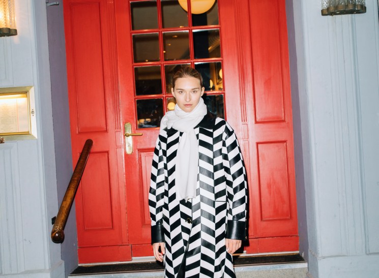 Model in black and white chevron coat with white turtleneck standing on steps outside restaurant Lumiere
