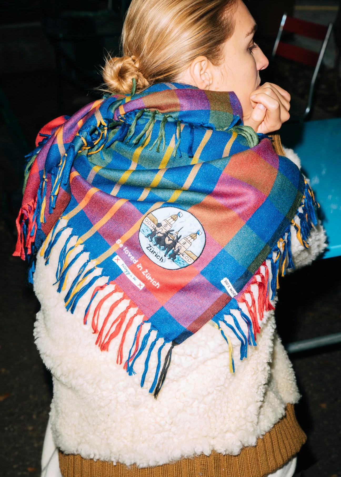 Model wearing layered winter fashion with colorful fringed scarf over white fluffy jacket