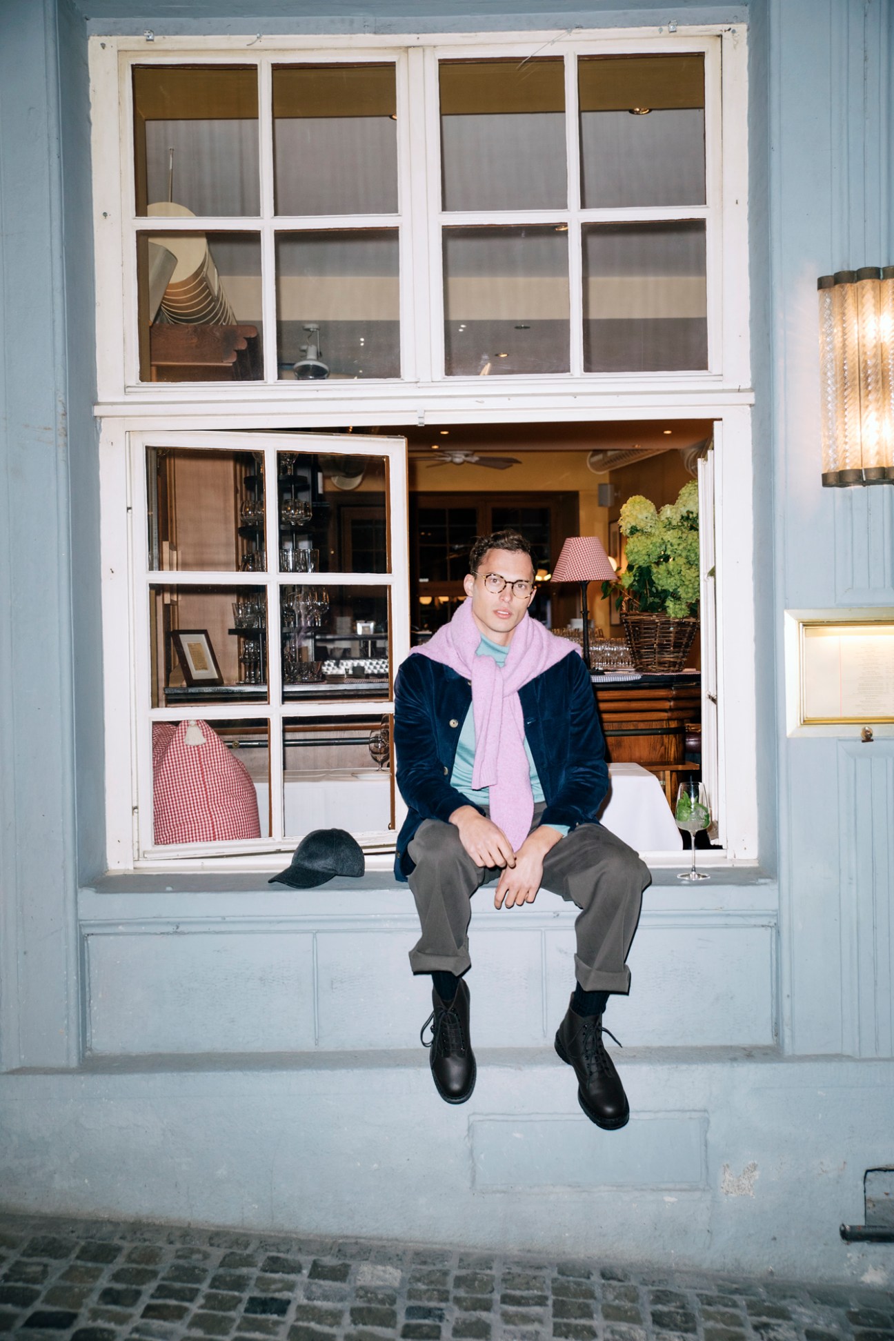 Male model wearing dark jacket with lilac scarf sitting in restaurant window