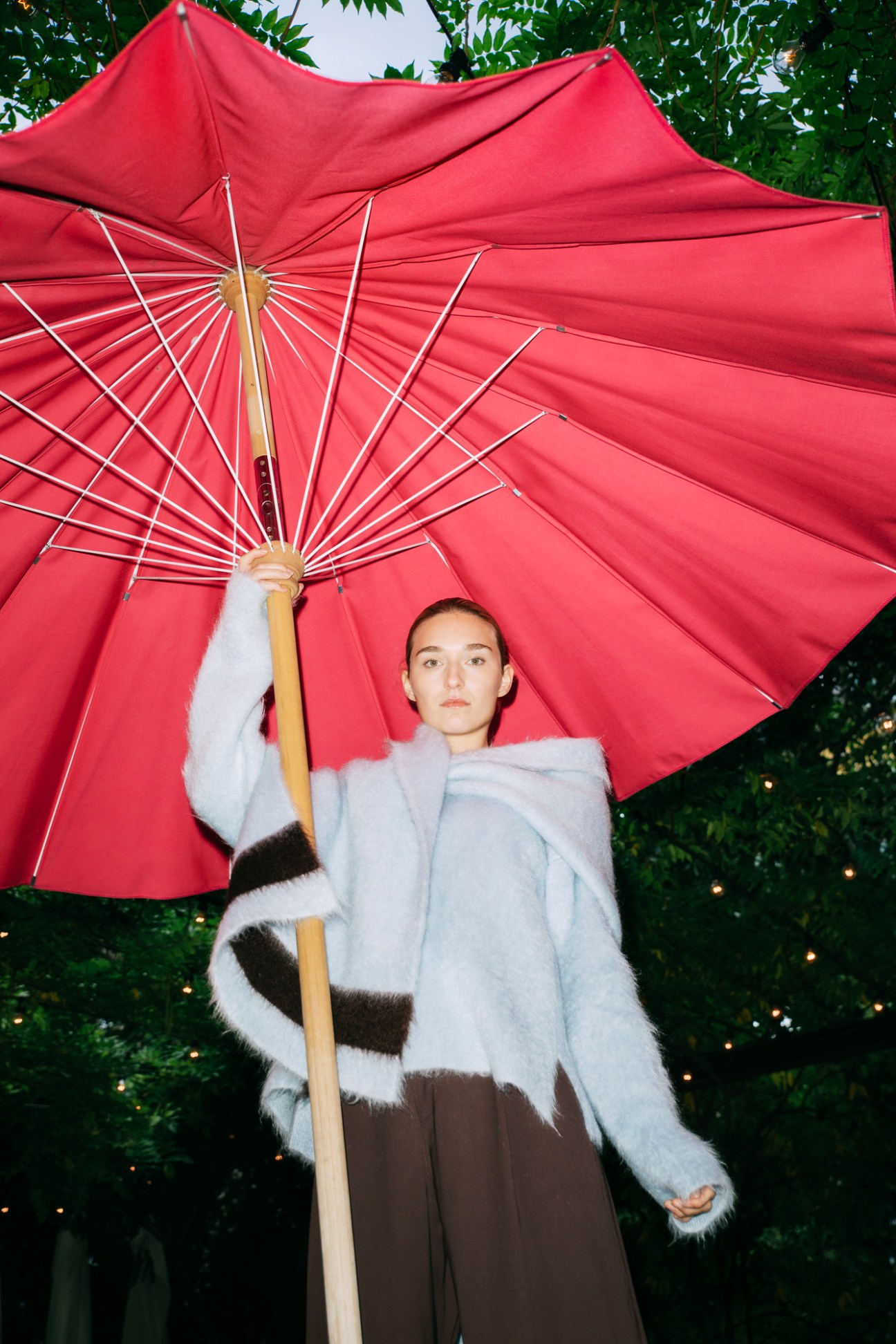 Model wearing Jil Sander collaboration jumper and scarf with Studio Nicholson trousers, holding red umbrella outdoors
