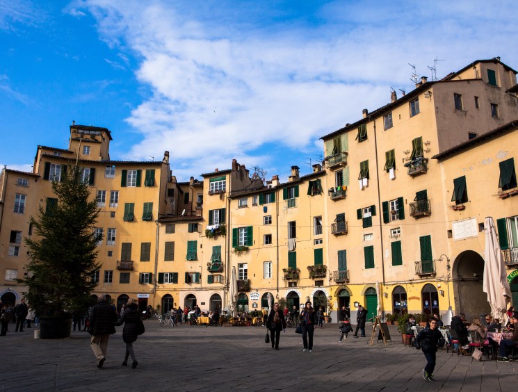 Curved Italian piazza lined with yellow buildings and green shutters.