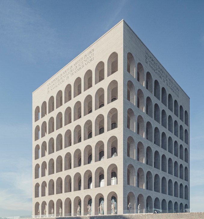 White travertine building with repetitive arched windows arranged in a cubic geometric pattern against blue sky