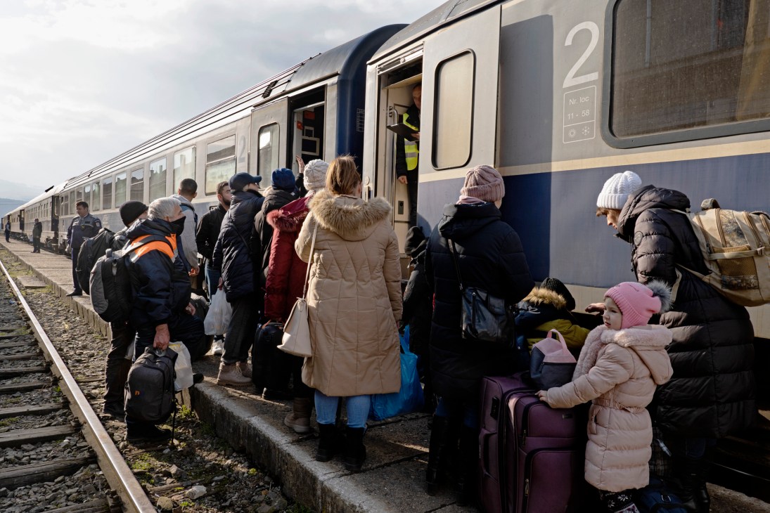 Refugees with luggage and children struggling to board an overcrowded train at a railway station