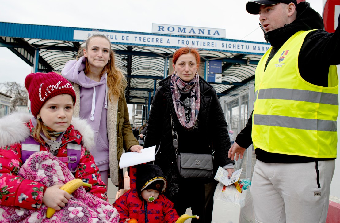 Family with children and luggage at Romanian border crossing with official in high-visibility vest