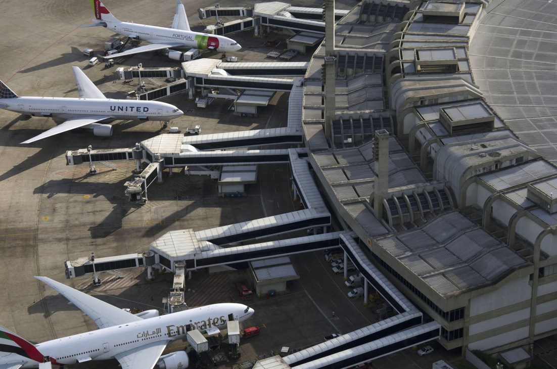 Aerial view of airport terminal with parked aircraft including United and Emirates planes at gates.