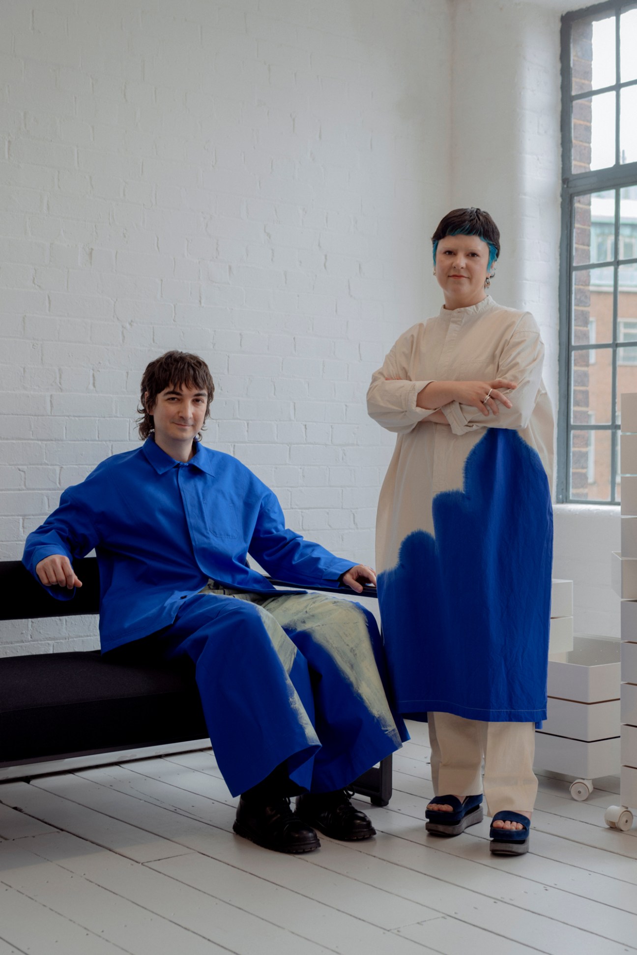 Two people in Japanese fashion styling wearing layered blue and cream garments in minimal showroom setting
