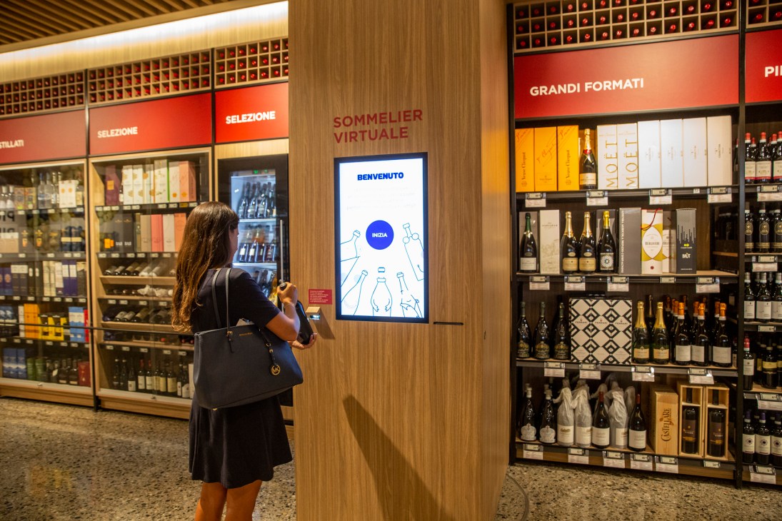 Woman using digital sommelier screen at modern wine store with extensive bottle selection