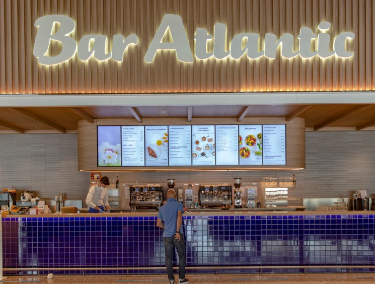 Modern coffee bar with illuminated Bar Atlantic signage, blue tiled counter, and digital menu displays overhead