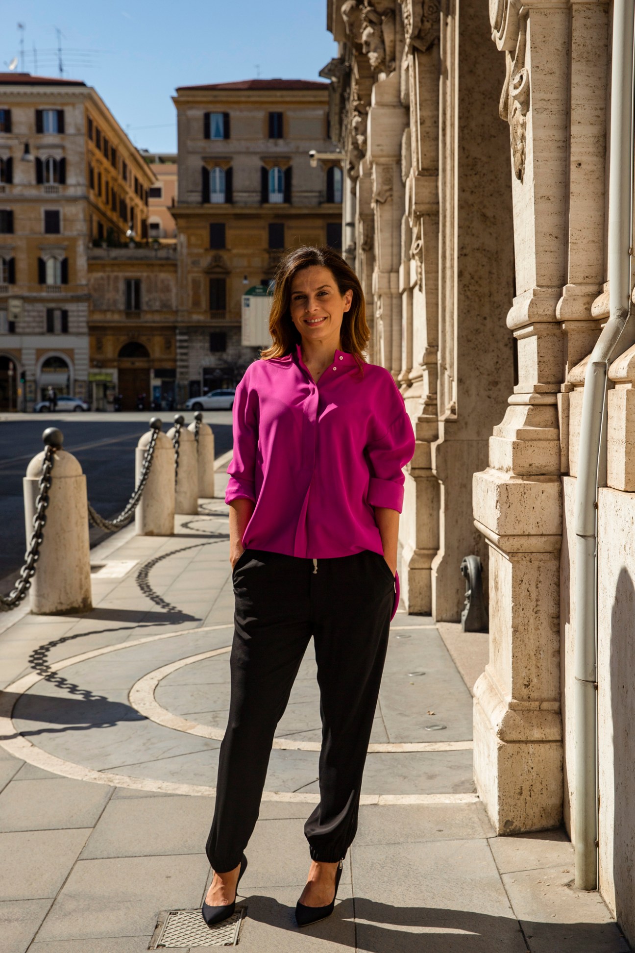Portrait of Francesca Bria standing in bright pink shirt against classical stone columns in Rome