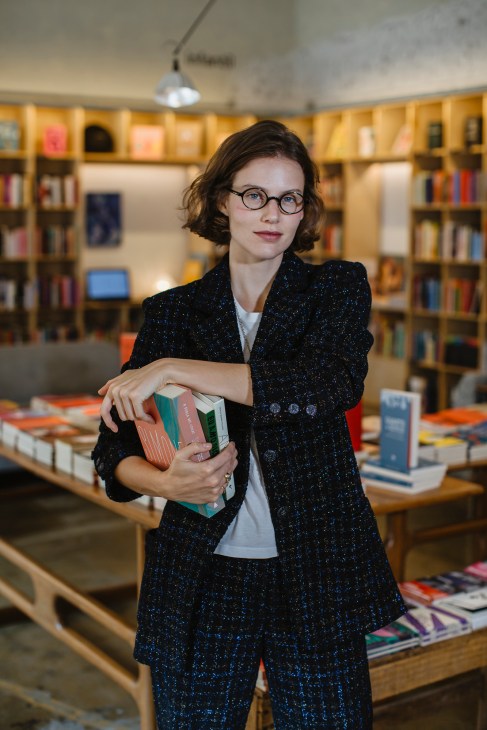 Johanna Stein, founder of Gato Sem Rabo bookshop, holds books in her São Paulo store with wooden shelves.