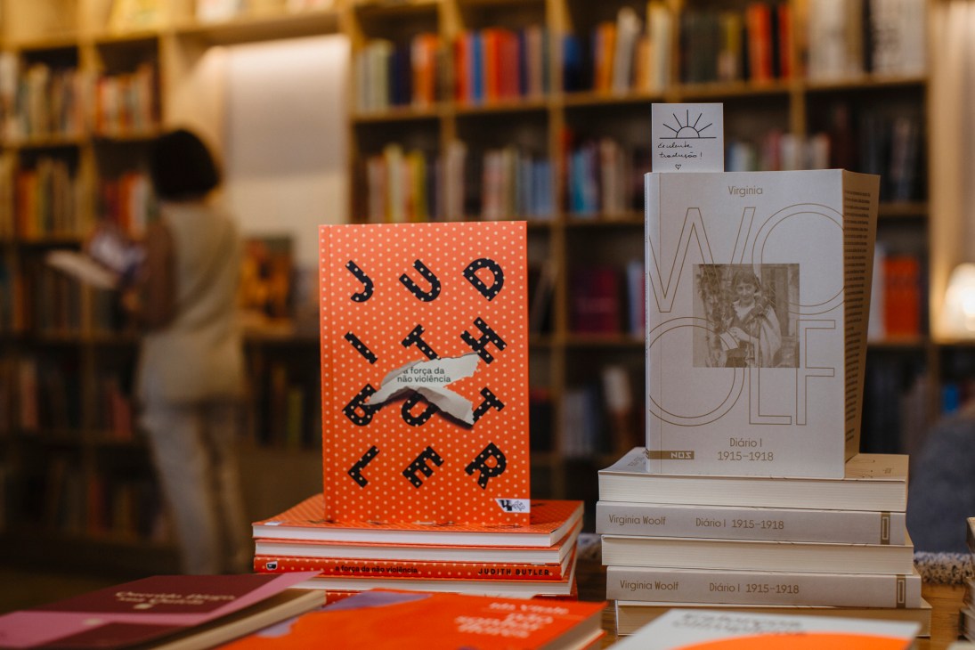 Stack of books displayed in Gato Sem Rabo bookstore with shelves of books blurred in background.