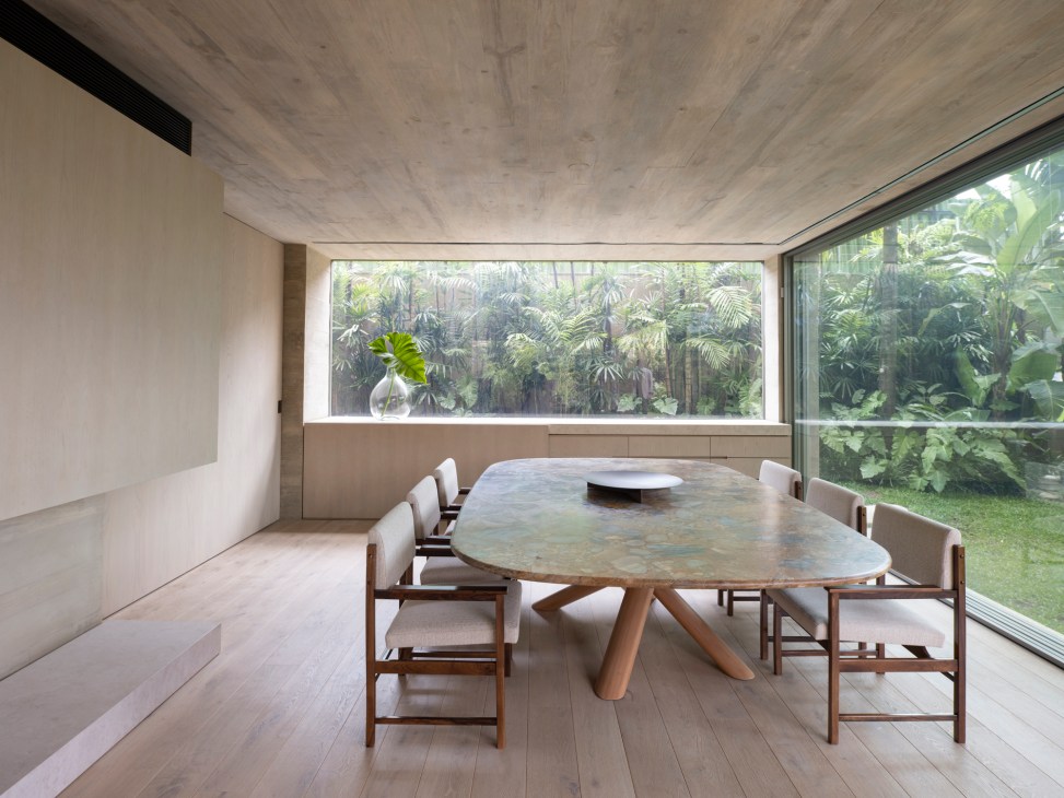 Modern dining room with oval marble table, wooden chairs and large windows overlooking tropical vegetation