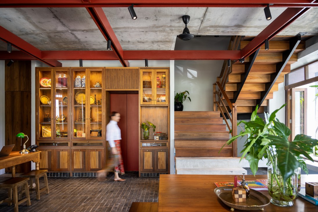 Modern interior with exposed concrete ceiling, red steel beams, wooden display cabinets, and floating staircase