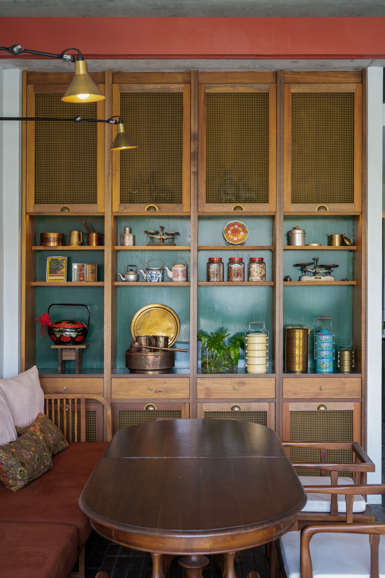 Wooden dining table with built-in shelving displaying vintage kitchen items and brass lighting fixtures