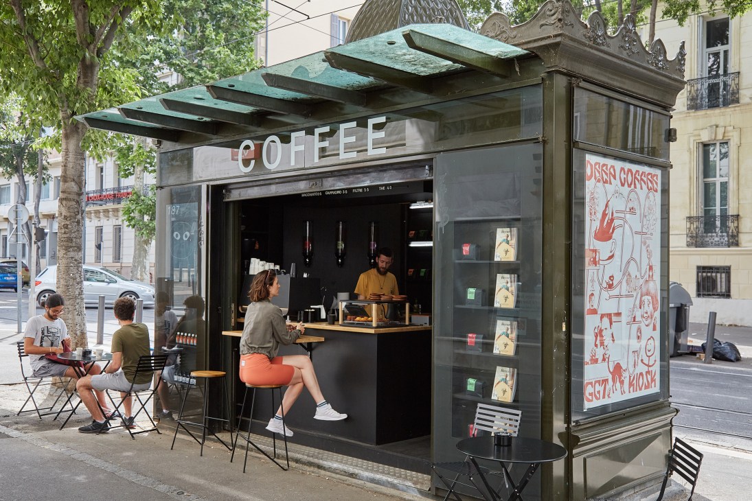 Modern coffee kiosk with glass panels and green roof serving customers at outdoor seating