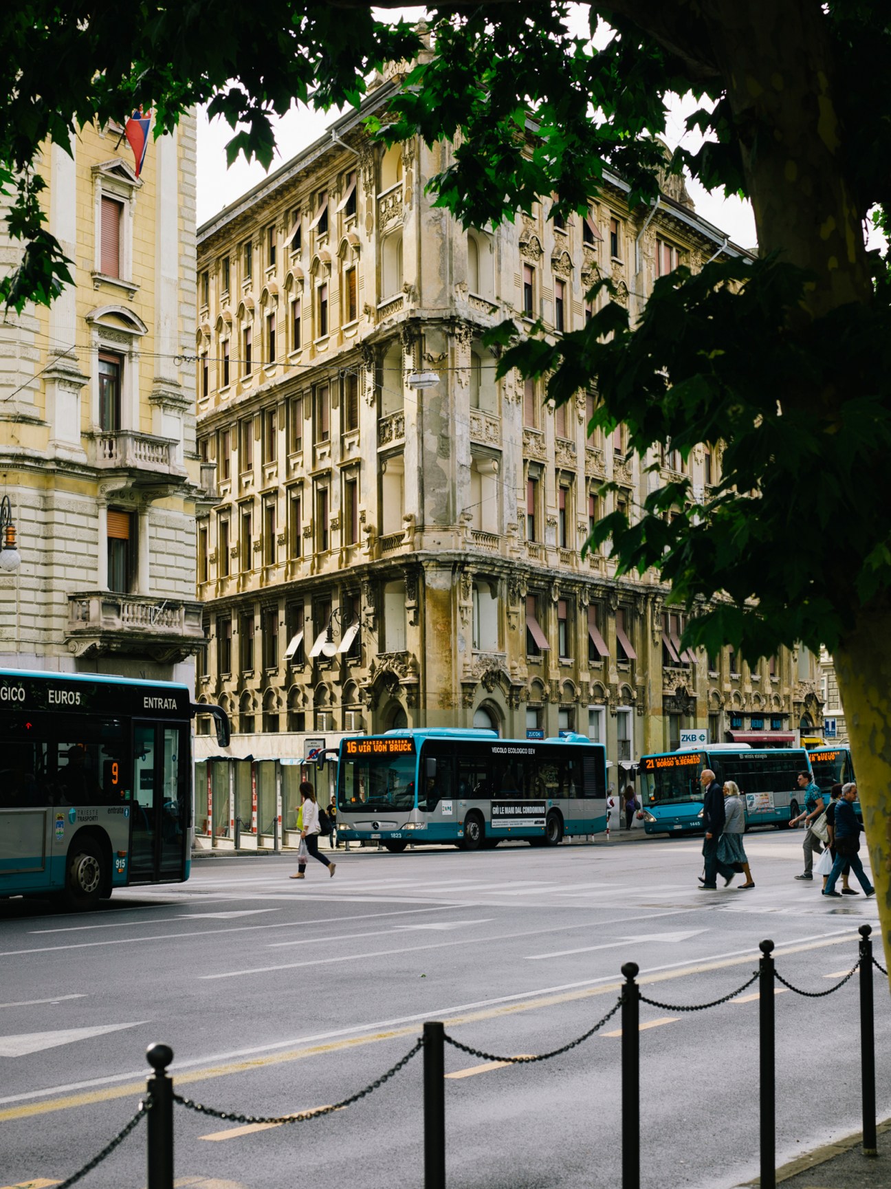 Barcelona street with historic neoclassical buildings, blue buses, and pedestrians crossing.
