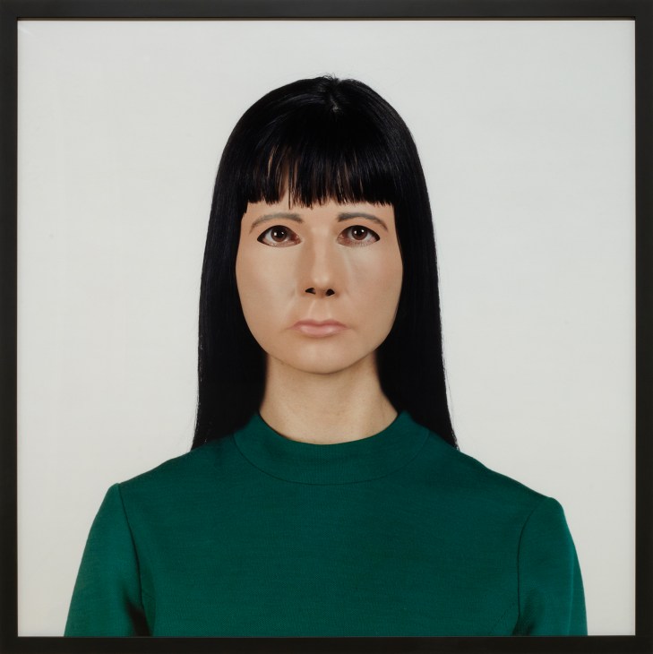 Portrait of a woman with black bob haircut and bangs wearing a green top against a white background