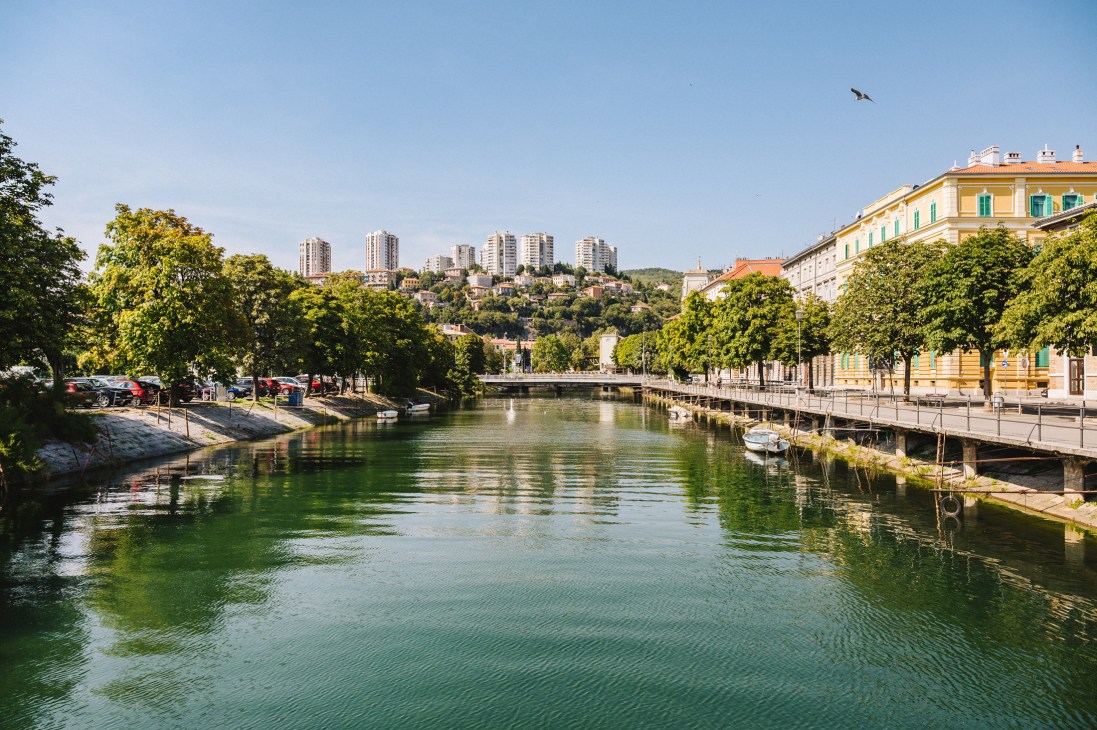 The Rjecina river flowing through Rijeka with colorful buildings lining both sides and hills in the background