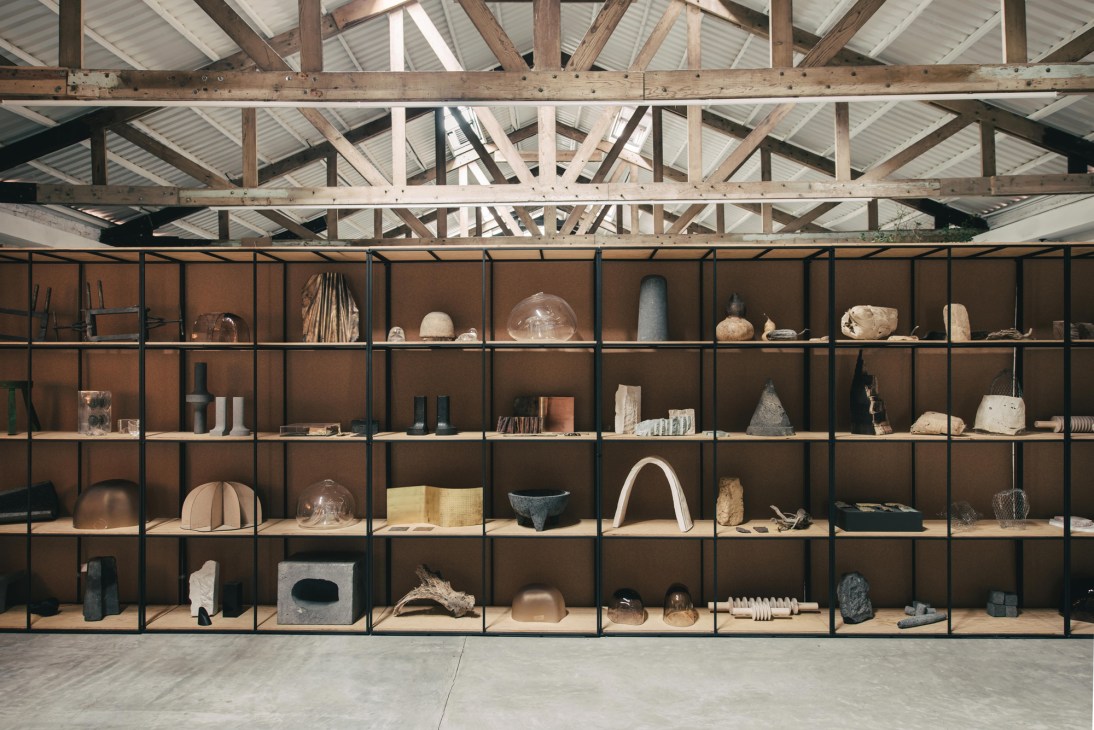 Large industrial shelving unit with black metal frame and natural wood shelves displaying sculptural objects and ceramics.