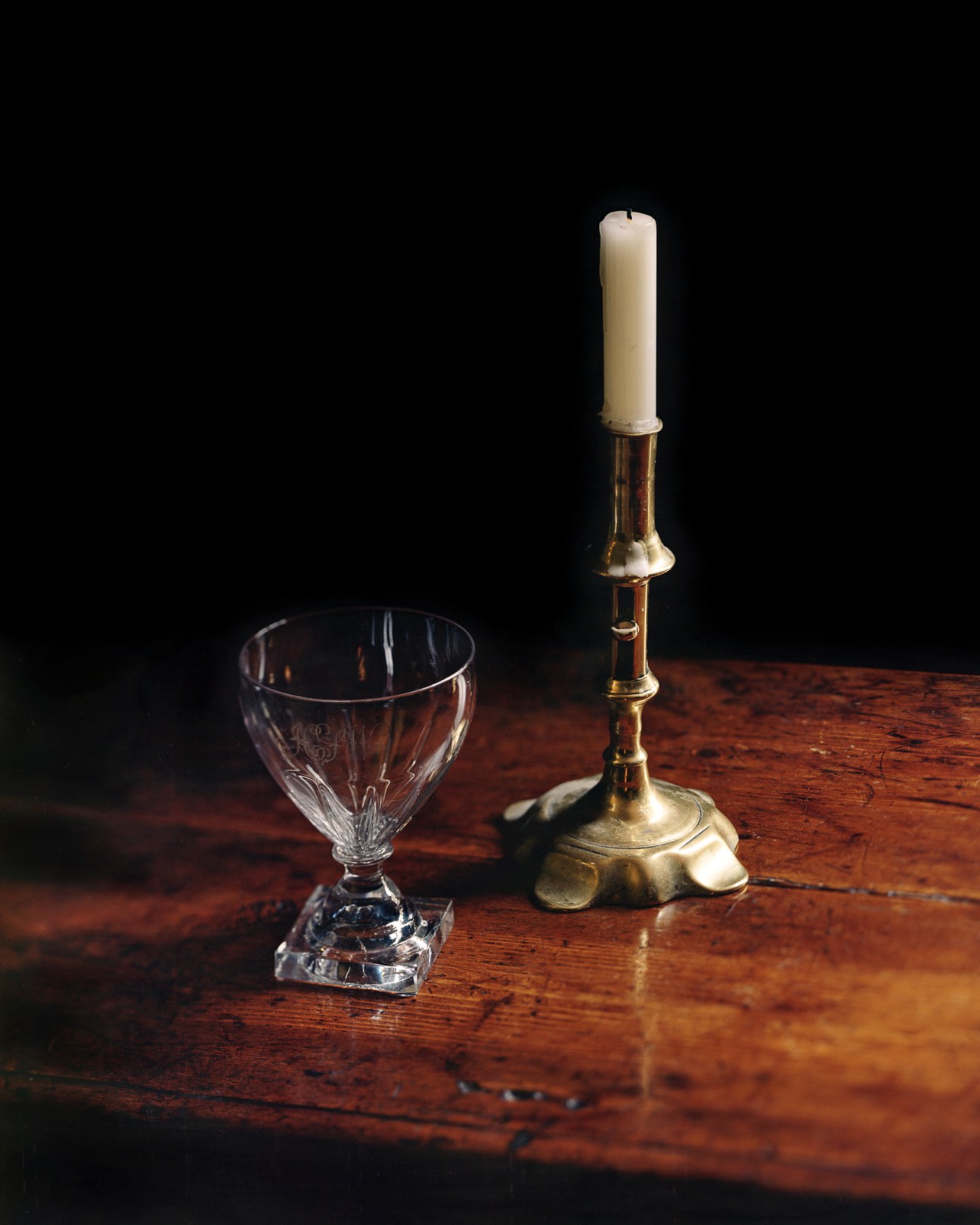 Georgian rummer glass drinking vessel on wooden surface beside brass candlestick with white candle